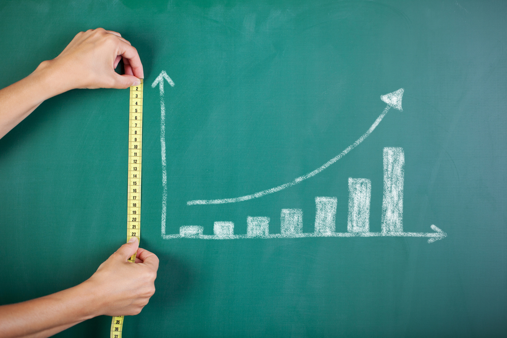 Closeup of woman's hands measuring bar graph with tape on blackboard